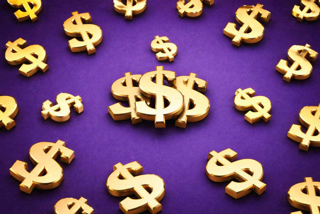 Złote znaki dolara rozsypane na fioletowym tle, symbol obfitości, pieniędzy i niezależności oraz tego czym jest wolność finansowa.