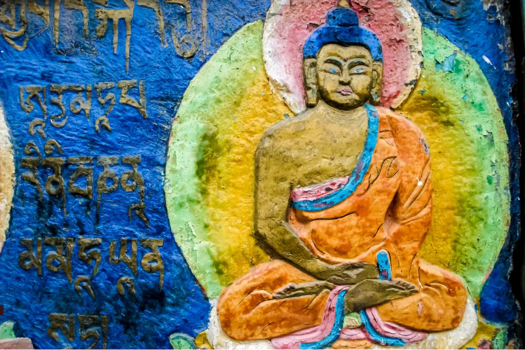 Płaskorzeźba Buddy siedzącego w pozycji medytacyjnej z aureolą i pokazującego jak medytować. Obok widoczne tybetańskie inskrypcje.