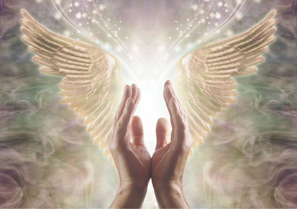 Wzniesione dłonie w geście anielskich afrimacji. Nad nimi są skrzydła anioła, a w tle jasna poświata.