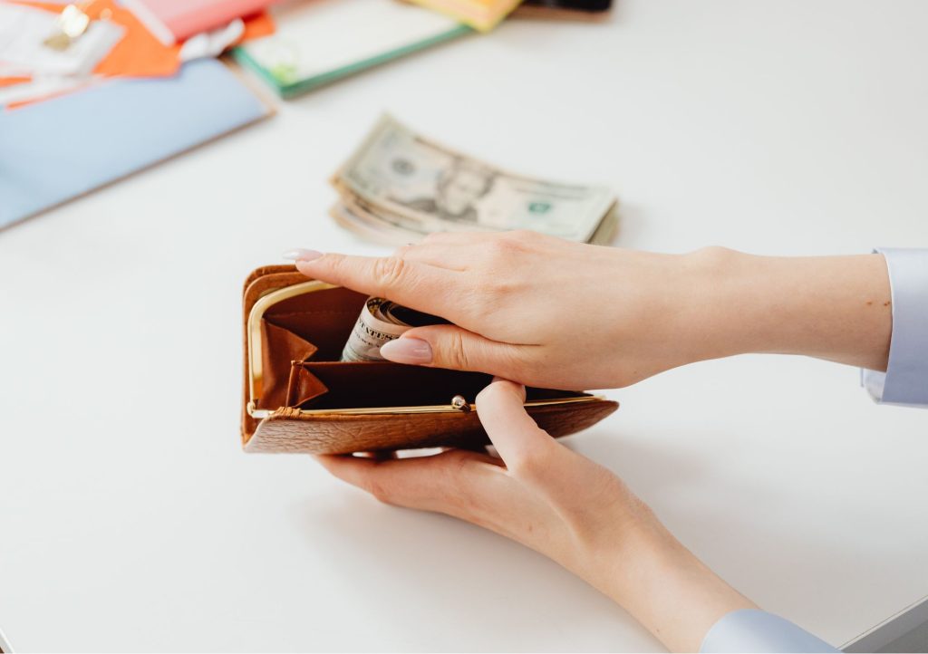 Dłonie trzymające pieniądze i skórzany portfel.