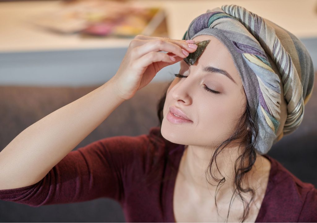 Kobieta w turbanie przykłada trójkątny kamień do czakry trzeciego oka.